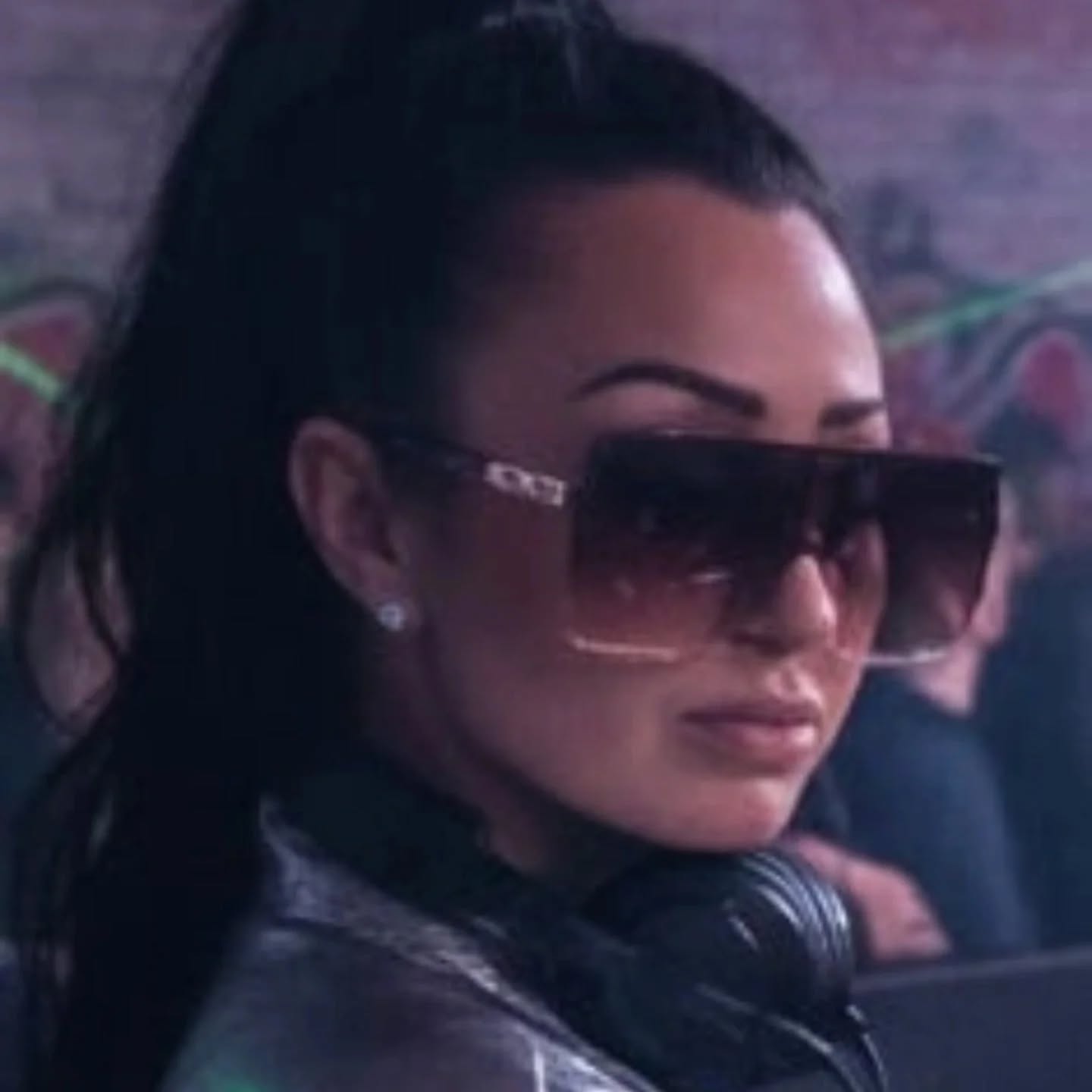 Skyza behind the decks, wearing oversized sunglasses with headphones around her neck